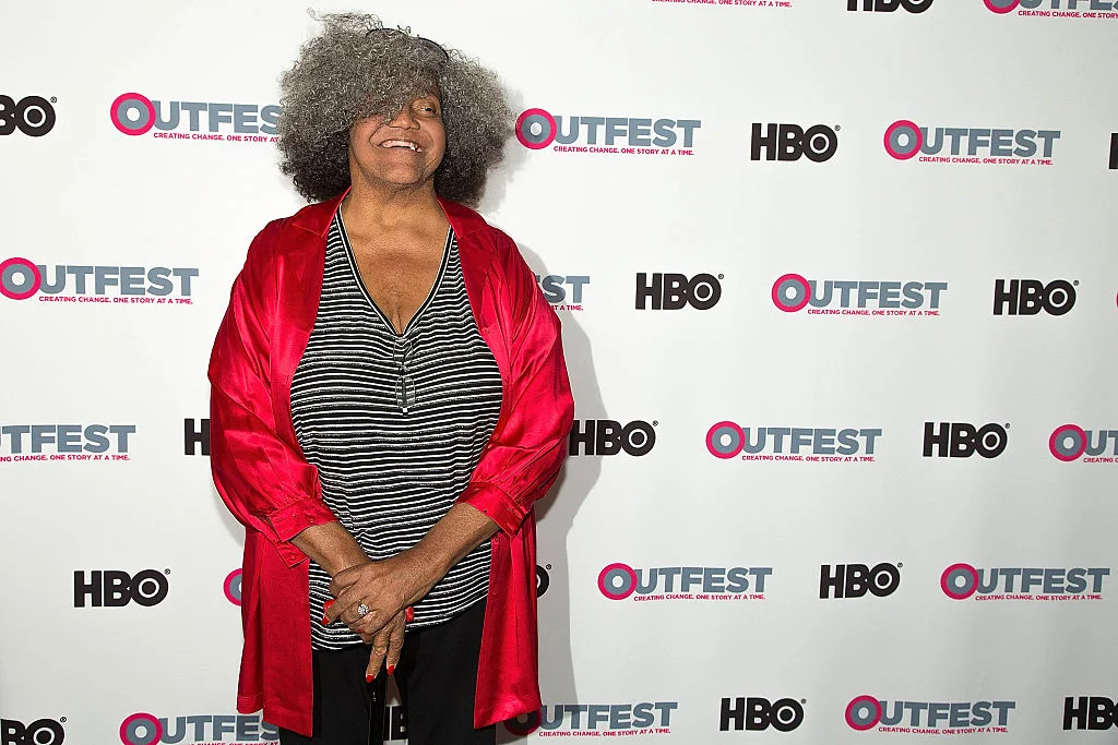 Miss Major wears a red satin cardigan over a blackandwhite striped shirt on the red carpet.